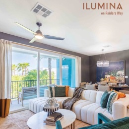 Luminous spaces await you at Ilumina, including our sun-soaked living rooms with oversized glass sliding patio doors.  #LiveIluminaRaidersWay #HendersonLVLiving Living room with a balcony at Ilumina at Raider's Way apartments in Henderson, NV