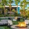 a courtyard with chairs and tables and a fire pit with palm trees and a building in the background
